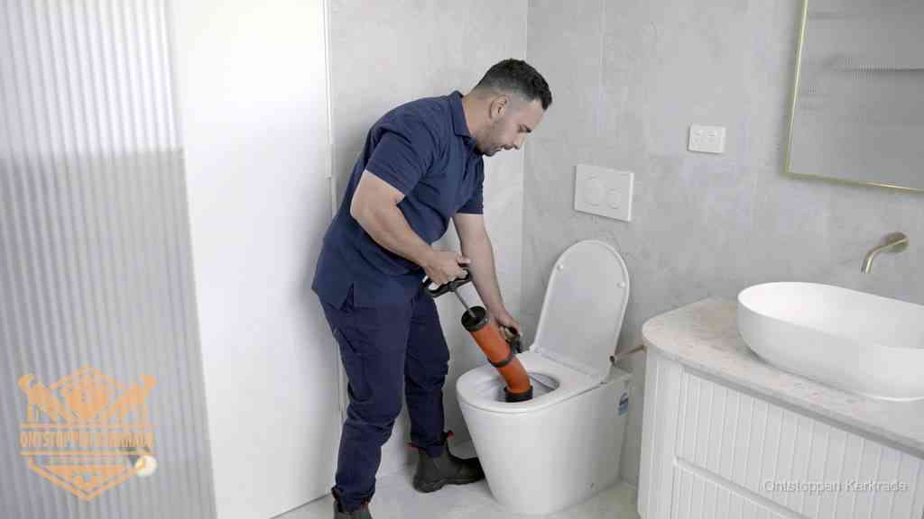 Een monteur buigt over een wandcloset en duwt met de hand een persluchtontstopper in de toiletpot om de verstopping handmatig los te maken in Kerkrade