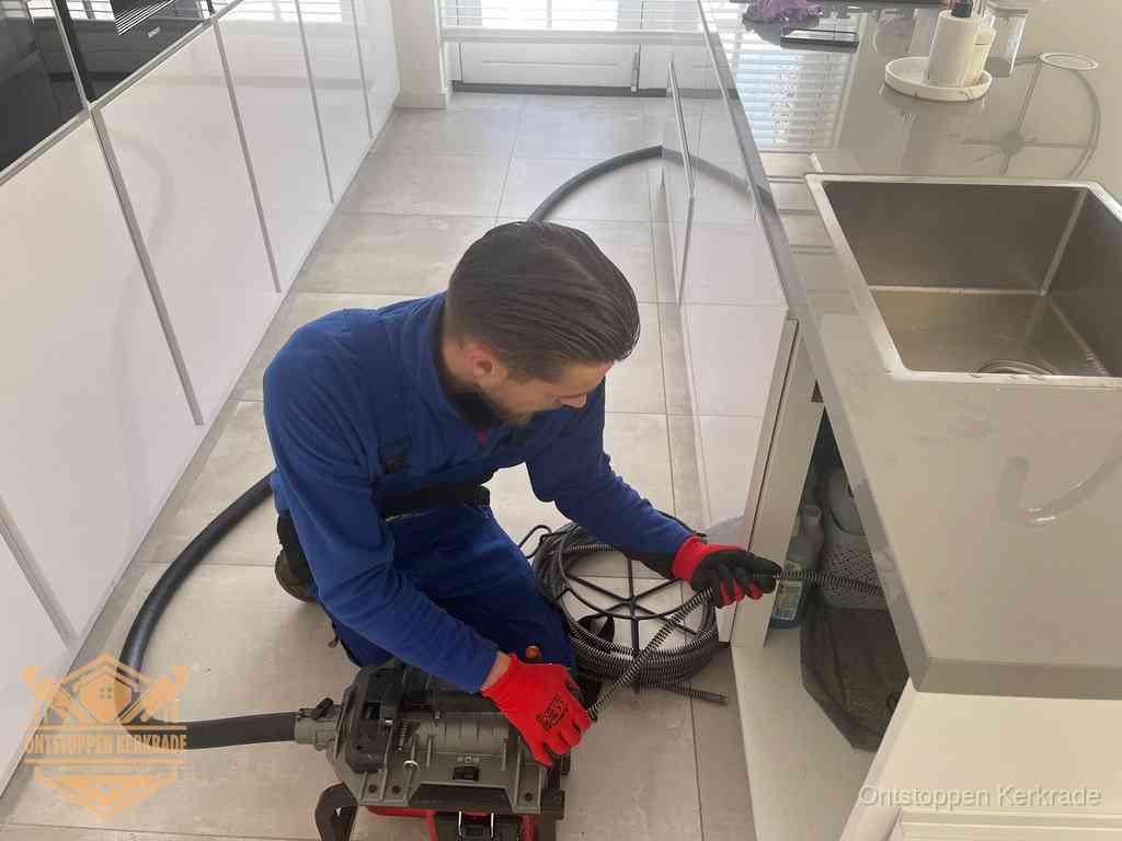 Een monteur ontstopt de keukenafvoer onder de spoelbak met een elektrische veermachine in Kerkrade