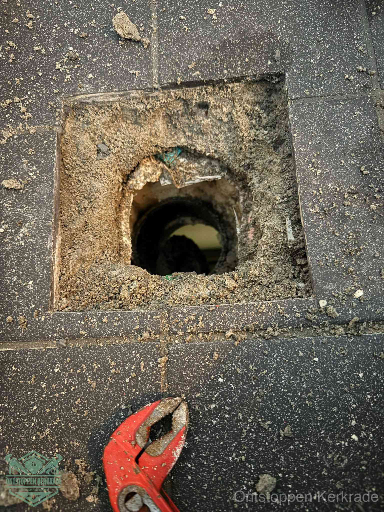 Een geopend rioolputje in een betontegelvloer met losgemaakt rooster en een zichtbare ronde afvoerbuis, het achterhalen waar de afvoerverstopping zit in Kerkrade
