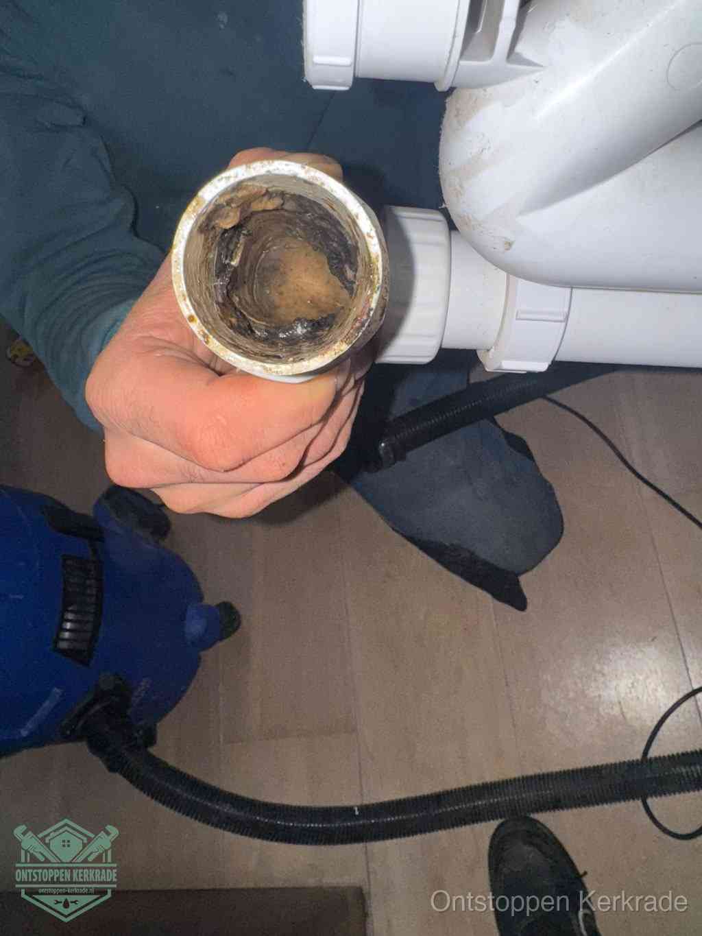 Een hand houdt een losgekoppeld PVC-afvoerbuisstuk vast dat van binnen volledig is dichtgeslibd met vet, vuil en aanslag, de meest voorkomende oorzaak van een verstopte afvoer in Kerkrade