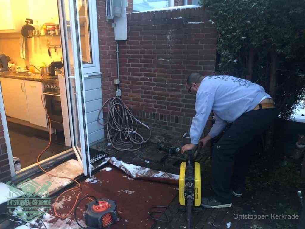 Een monteur werkt buiten bij een open riool-/grondput met een elektrische ontstoppingsmachine om een verborgen afvoerprobleem op te sporen in Kerkrade