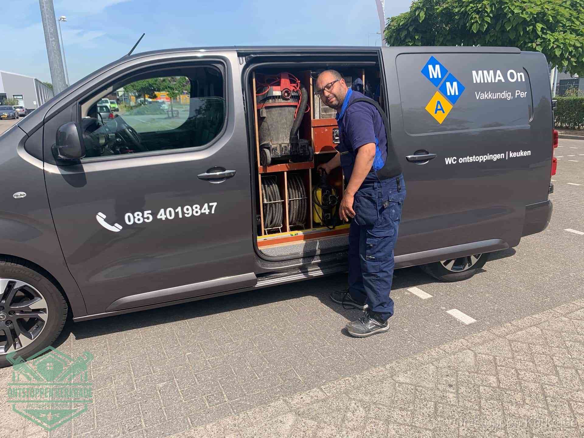 Een monteur bij de open schuifdeur van zijn bedrijfsbus op een parkeerplaats, klaar om de oorzaak van terugkerende afvoerverstoppingen aan te pakken in Kerkrade