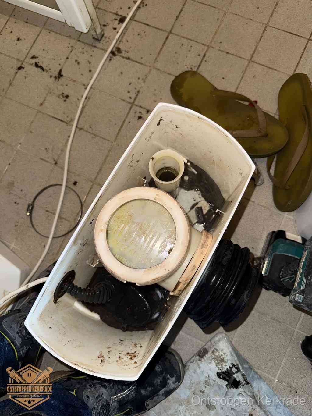 Een gedemonteerde toiletpot op de vloer met ontstoppingsveer en gereedschap ernaast, het verwijderen van een vastzittend voorwerp uit de wc in Kerkrade