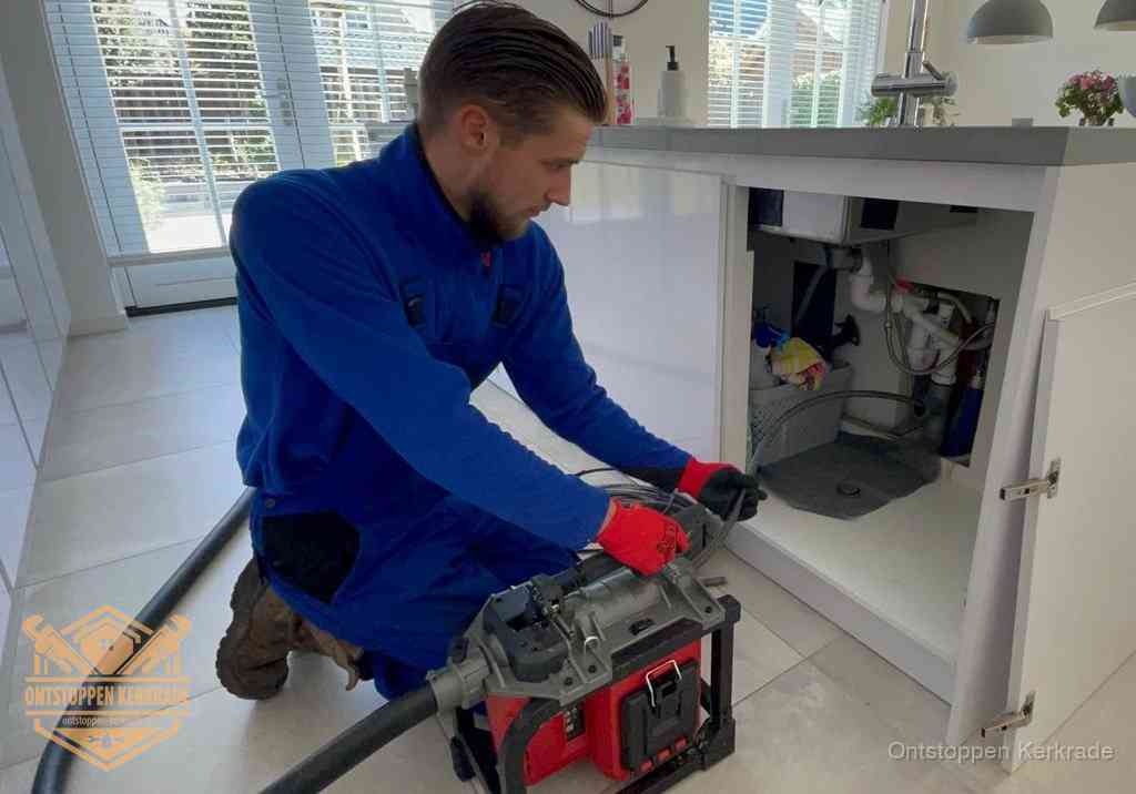 Een monteur voert een professionele elektrische ontstoppingsmachine in de afvoer onder de spoelbak tijdens het gootsteen ontstoppen in Kerkrade
